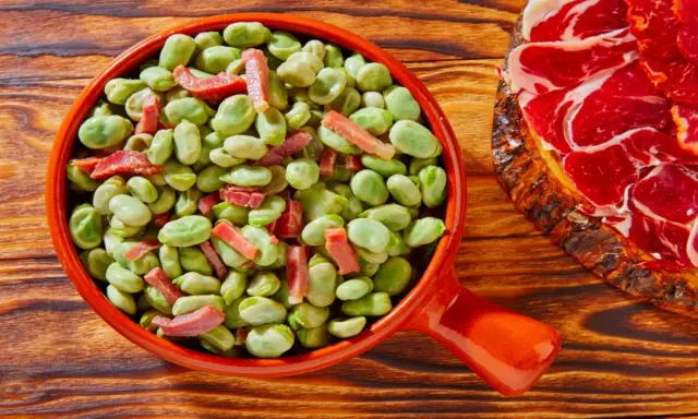 Un plato de habas tiernas con trocitos de jamón, ideal para quienes preguntan qué es el favismo y buscan recetas.