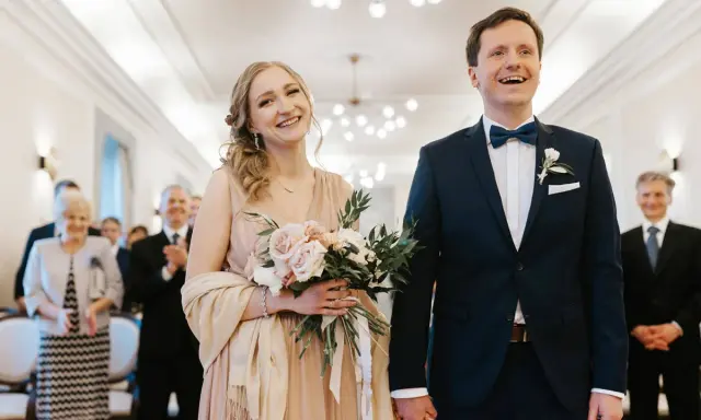 Para młoda uśmiecha się radośnie, trzymając bukiet. Złożyli wniosek o ślub cywilny i są gotowi na ceremonię.