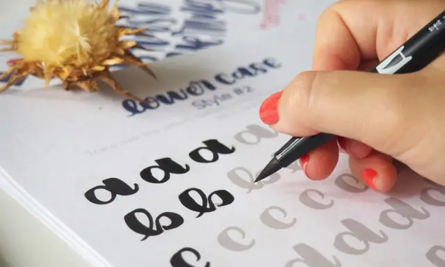 Mano practicando cómo hacer lettering con un rotulador sobre un papel con letras de ejemplo.