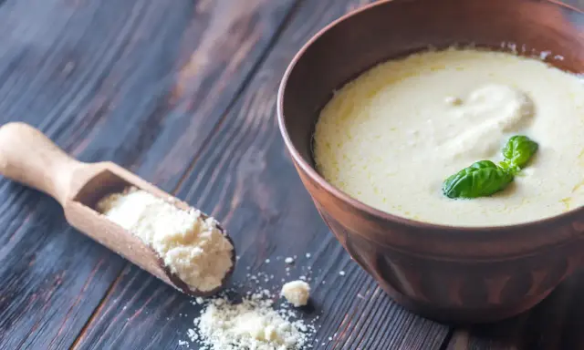 Sauce crémeuse à la sauce parmesan italienne, garnie de basilic frais. Une cuillère en bois contient du parmesan râpé.