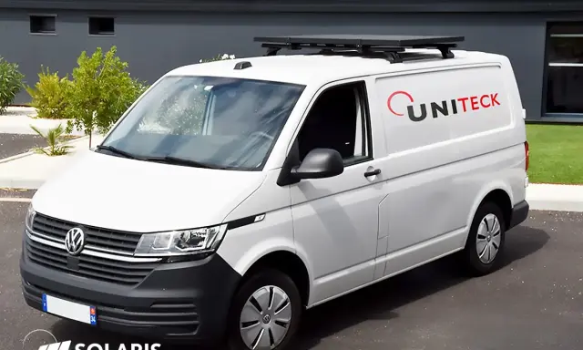 Un fourgon blanc avec un panneau solaire sur barre de toit. Le logo UNITECK est visible sur le côté.