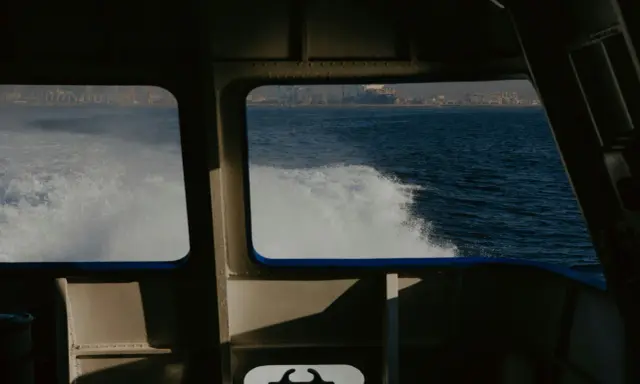 Vue depuis la cabine d'un bateau, avec le sillage blanc de l'eau. Au loin, une ville côtière et des grues de port. Les canaux VHF marine sont essentiels pour la communication.