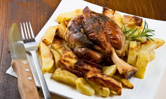 Stinco di maiale arrosto con patate croccanti, guarnito con rosmarino fresco. Un piatto succulento pronto per essere gustato.