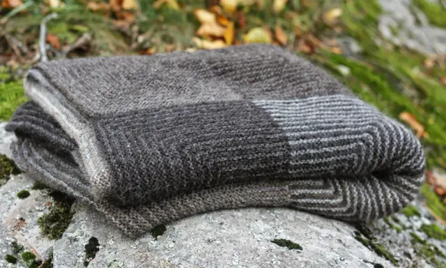 En hopvikt, handstickad filt i gråa nyanser ligger på en mossig sten. Perfekt för mysiga höstkvällar.