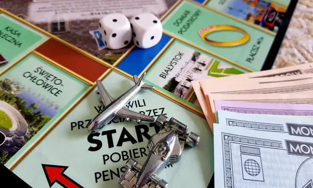 Gra Monopoly, kostki, pionki (samolot, bolid), pieniądze i plansza z polskimi miastami. Różne rodzaje gry wciągają graczy w świat finansów.