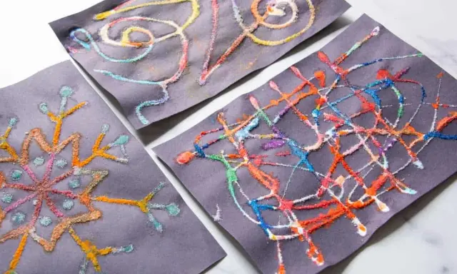 Kinder malen auf schwarzem Papier mit bunten Salzkristallen. Ein Bild zeigt eine Schneeflocke, die anderen abstrakte Muster.