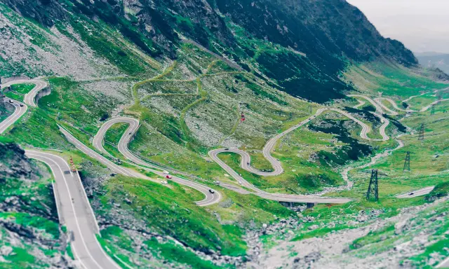 Kręta droga Transalpina wijąca się po zielonych zboczach gór. Widok z lotu ptaka na serpentyny i mosty.