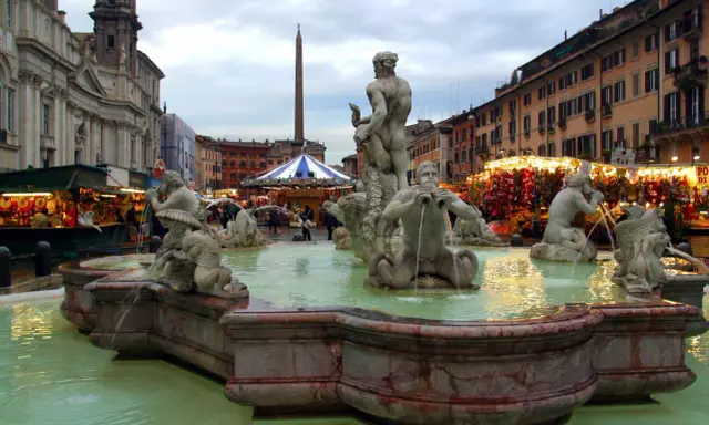 Fontana dei Quattro Fiumi a Piazza Navona, Roma, con bancarelle illuminate che anticipano quando iniziano i mercatini di Natale a Roma.