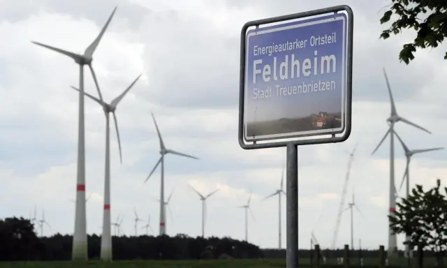 Schild "Energieautarker Ortsteil Feldheim, Stadt Treuenbrietzen" vor vielen Windrädern in Brandenburg.