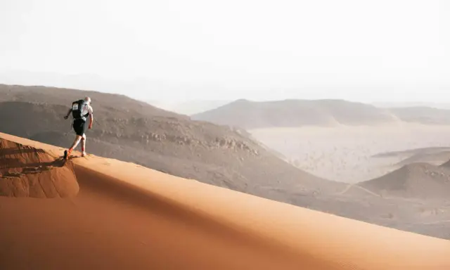 Läufer erklimmt eine Sanddüne, bereit für den Marathon des Sables. Die Wüstenlandschaft erstreckt sich in der Ferne.
