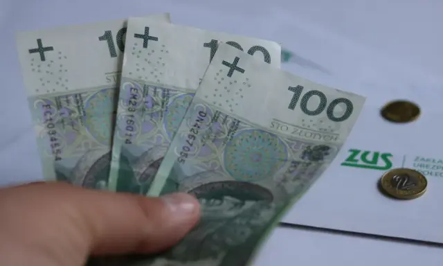 Trzy stuzłotowe banknoty w dłoni, obok dokument ZUS i monety. Czy to 30 krotność zus 2025?