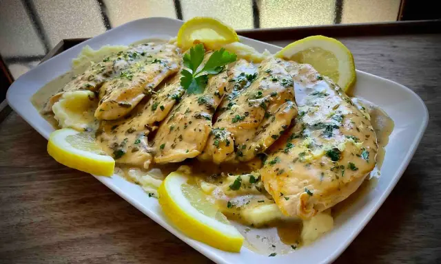Delicioso pollo al limón con puré de patatas, adornado con rodajas de limón y perejil fresco.