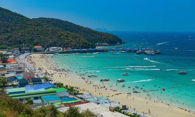 Ein belebter Pattaya Strand mit vielen Menschen, Sonnenschirmen und Booten im türkisfarbenen Meer.