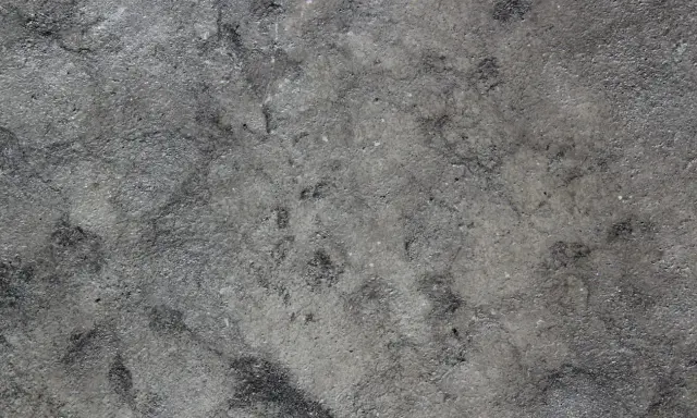 Textura rugosa y desigual de hormigón gris, con zonas más oscuras que sugieren desgaste o humedad.