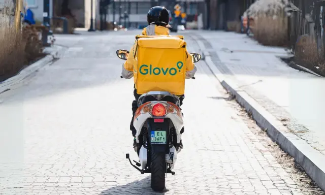 Kurier Glovo na skuterze, w żółtej kurtce z logo, przemierza ulicę. Zastanawiasz się, ile zarabia pracownik Glovo?