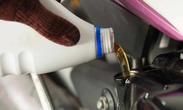 Rękawica nalewa nowy olej do silnika motocykla podczas wymiany oleju.