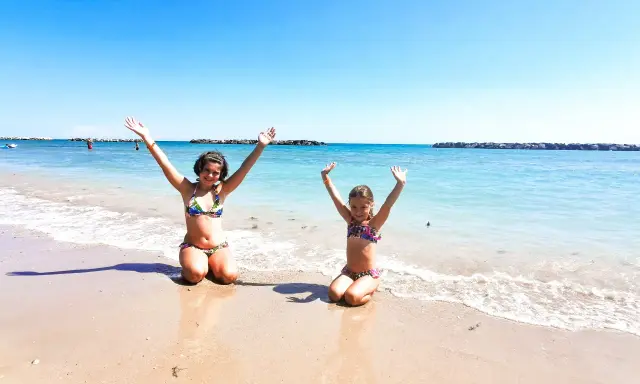 Due bambine felici sulla spiaggia del villaggio Riva Verde, Marche, con le braccia alzate verso il cielo azzurro.