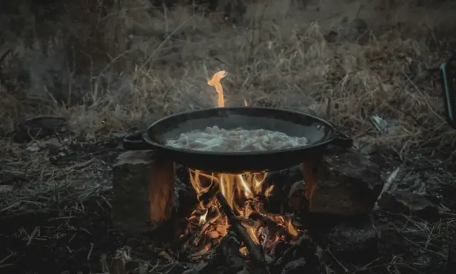 Cuisine en plein air sur un réchaud rocket stove improvisé. Une poêle cuit des aliments sur un feu vif.