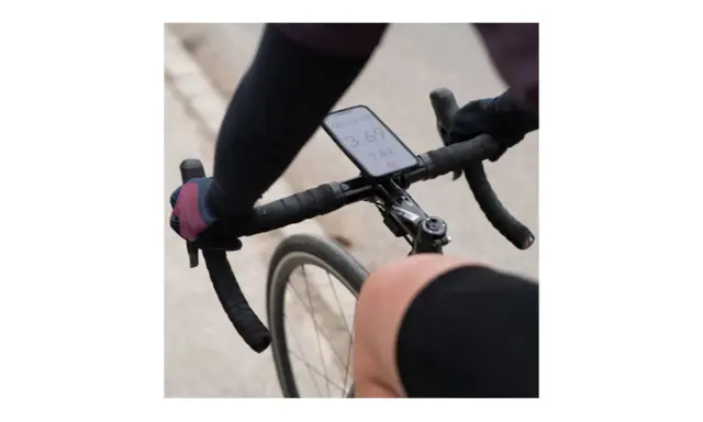 Rowerzysta trzyma kierownicę, na której zamontowano telefon za pomocą uchwytu sp connect. Na ekranie widoczny czas i prędkość.