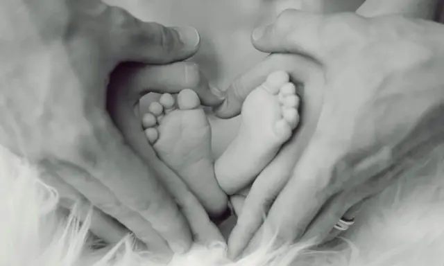 Manos de padre formando un corazón alrededor de los pies de su bebé, un símbolo de apego excesivo al padre y amor incondicional.