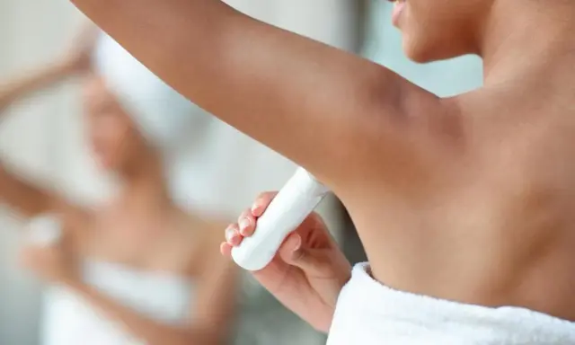Une femme applique un déodorant sous ses aisselles. L'acide glycolique peut aider à éclaircir les aisselles.