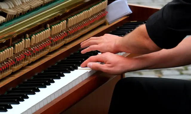 Mains sur le clavier d'un piano, prêt à jouer d'un instrument. Les marteaux et les cordes sont visibles.
