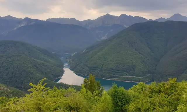 Valli boscose e un lago serpeggiante nella **Garfagnana e Lunigiana**, con montagne maestose sullo sfondo.