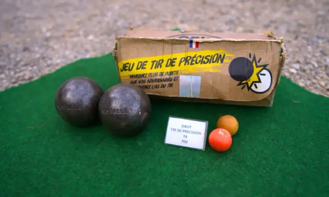 Deux boules de pétanque, un cochonnet et une boîte "Jeu de tir de précision" suggèrent un défi de poids et de diamètre pour le tireur.