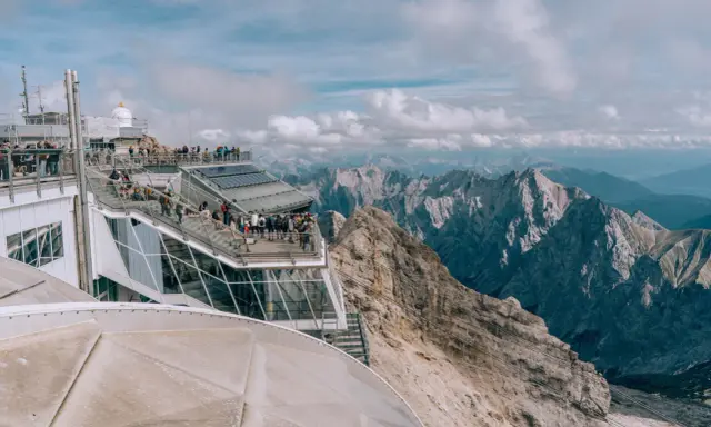 Tłum turystów na tarasie widokowym najwyższego szczytu Niemiec, Zugspitze, podziwia alpejskie krajobrazy.