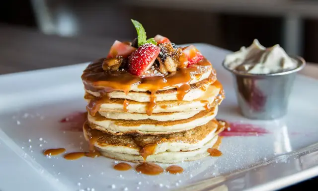 Pancakes con sciroppo d'acero, fragole e panna. Il dulcis in fundo significato di una colazione perfetta.