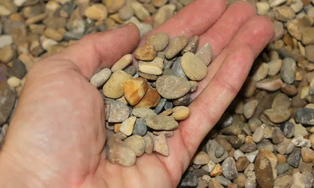 Mano sosteniendo una variedad de guijarros, mostrando que son los áridos, pequeños fragmentos de roca y minerales.