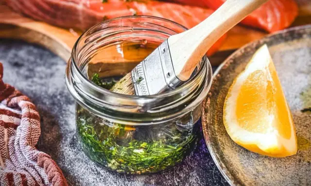 Marinade mit Kräutern und Zitrone bereit, um den Lachs zu verfeinern. Ein Pinsel liegt in der Glasflasche.