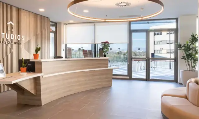 Recepción moderna y luminosa de living studios Alcobendas, con mostrador curvo, plantas y un sofá curvo.