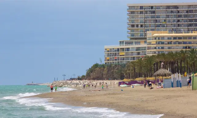 Menschen genießen den sonnigen torremolinos strand mit Palmen und einem großen Hotel im Hintergrund.