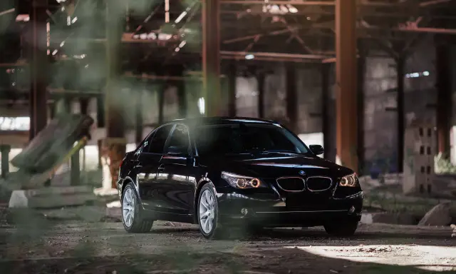 Czarny BMW 535d w opuszczonej hali, otoczony mgłą i gruzem.