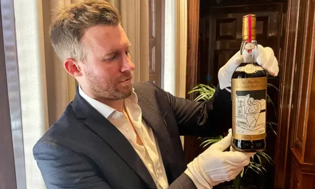 Mężczyzna w białych rękawiczkach prezentuje butelkę The Macallan 60 Year Old, jedną z najdroższych whisky świata.