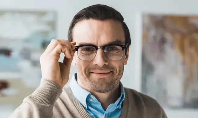 Mężczyzna w okularach dwuogniskowych poprawia je, uśmiechając się. Widać wyraźnie podział soczewek, jak wyglądają okulary dwuogniskowe.