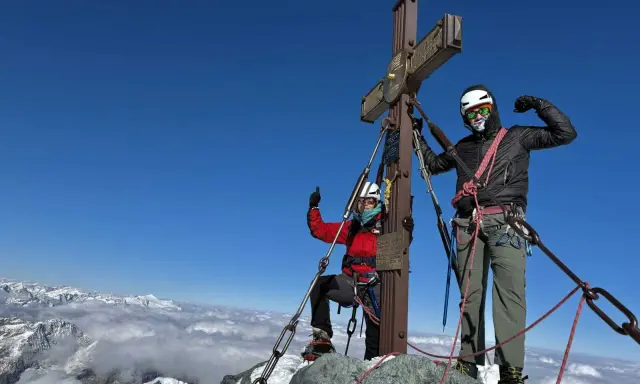Dwóch alpinistów na szczycie najwyższego szczytu w Austrii. Widok na góry i chmury poniżej.