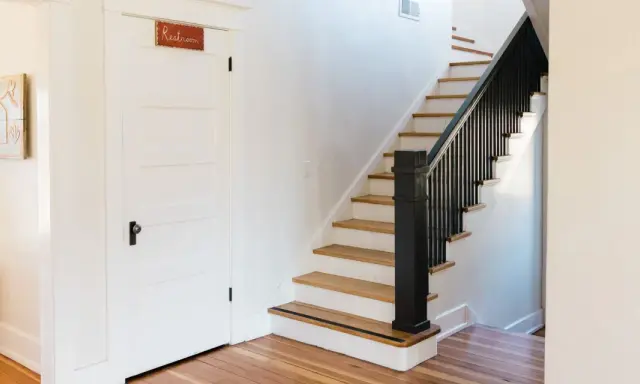 Escalier avec rampe noire, une idée couleur pour une cage d'escalier moderne. Une porte blanche avec un panneau "Restroom" est visible.