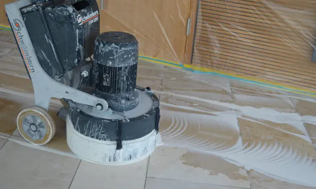 Bodenmaschine poliert Marmor. Staub und Wasser bilden Muster auf dem Boden, während die Maschine den Stein glänzend macht.