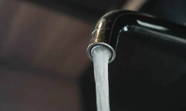 Un robinet chromé verse un jet d'eau. L'image évoque la dureté de l'eau par commune en France, un sujet important pour la vie quotidienne.