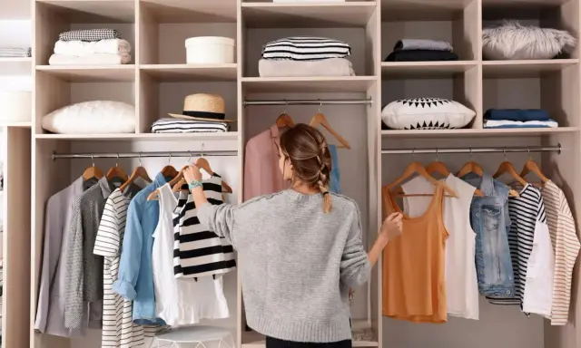 Kobieta porządkuje szafę, wieszając ubrania. Widać półki z poukładanymi rzeczami i wieszaki z odzieżą. To inspiracja, wie organisiert man den kleiderschrank.