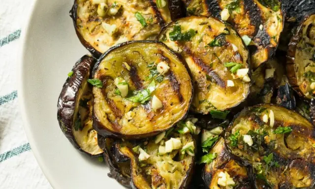 Aubergines grillées en rondelles, garnies d'ail et de persil, sur une assiette.
