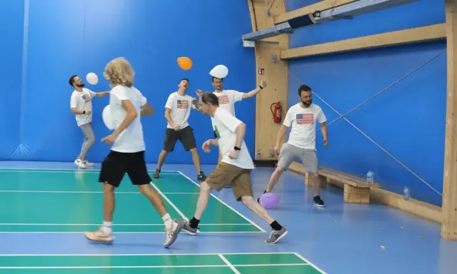 Mężczyźni w koszulkach z amerykańską flagą grają w gry zespołowe dla dorosłych, odbijając balony na hali sportowej.