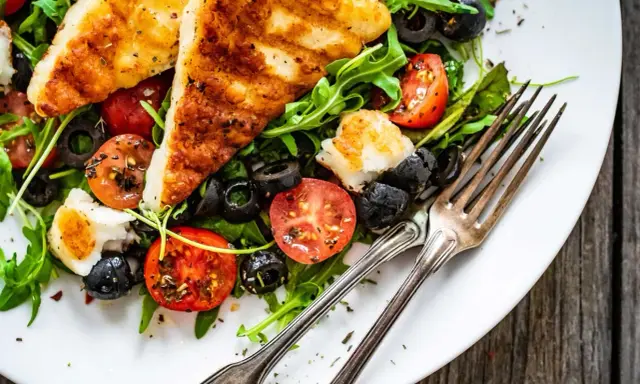 Pyszna sałatka z grillowanym halloumi, pomidorkami koktajlowymi i czarnymi oliwkami, podana z rukolą.