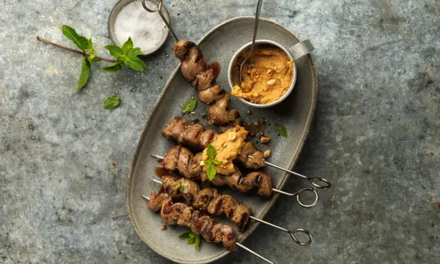 Brochettes d'agneau grillées au barbecue, servies avec une sauce aux arachides et garnies de menthe fraîche.