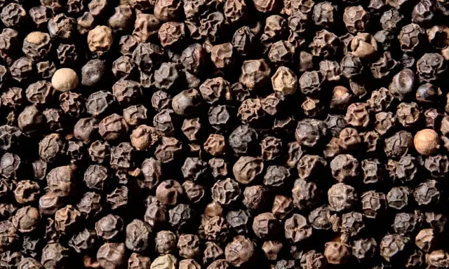Ziarna czarnego pieprzu, z jednym jaśniejszym. Czy pieprz jest zdrowy? Tak, zawiera piperynę, która wspomaga trawienie i ma właściwości przeciwzapalne.