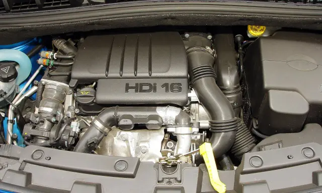 Silnik HDI 16 w Citroenie C4. Widoczny jest czarny plastikowy dekiel z napisem "HDI 16", przewody, rury dolotowe i inne elementy jednostki napędowej.
