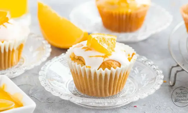 Fanta Muffins mit weißer Glasur und Orangenspalten, serviert auf kleinen Glastellern.
