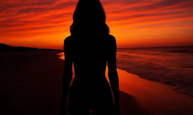 Silueta de una mujer en la playa al atardecer, con el cielo en tonos naranjas y rojos intensos.